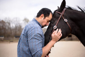 man in blue shirt hugs the face of a dark brown horse